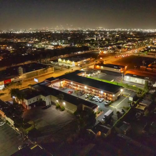 Aerial view of a cityscape at night showcasing illuminated buildings, streets, and distant lights on the horizon, with a parking lot in the foreground.