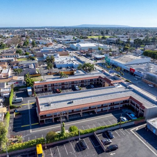 Aerial view of an urban area featuring a commercial complex, multiple residential buildings, streets, and parking lots under clear skies.