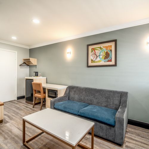 A modern room with a gray couch, coffee table, desk, chair, wall art, and an air conditioning unit. Simple and contemporary decor.