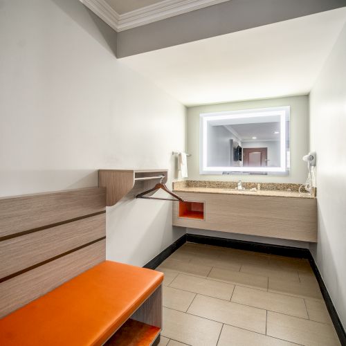 A modern, minimalistic changing or dressing room featuring a bench, coat hooks, and a countertop with a sink and mirror.