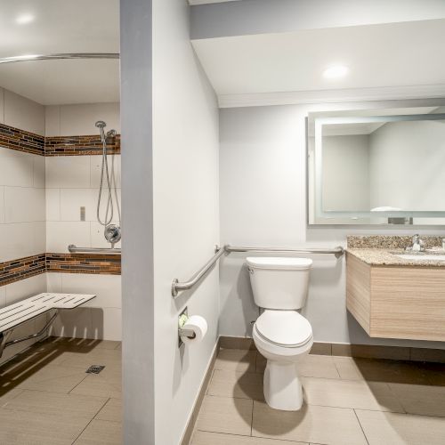 This image shows a clean, modern bathroom with a shower area, toilet, and a sink with a mirror above, all in neutral tones.