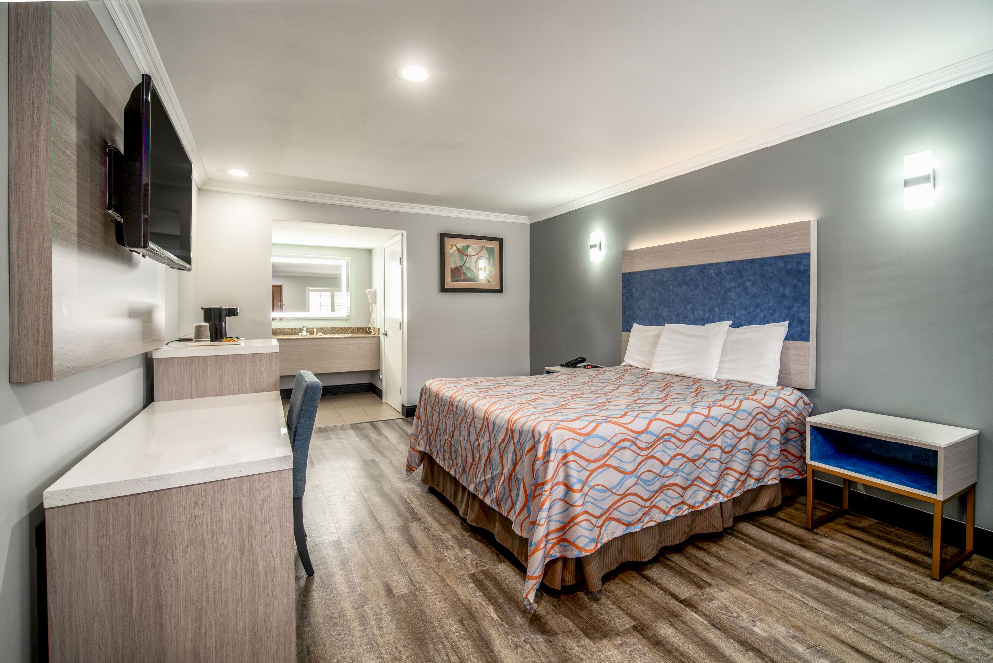 A modern hotel room with a double bed, television, desk, chair, and adjacent bathroom, featuring contemporary decor and a wooden floor ending the sentence.