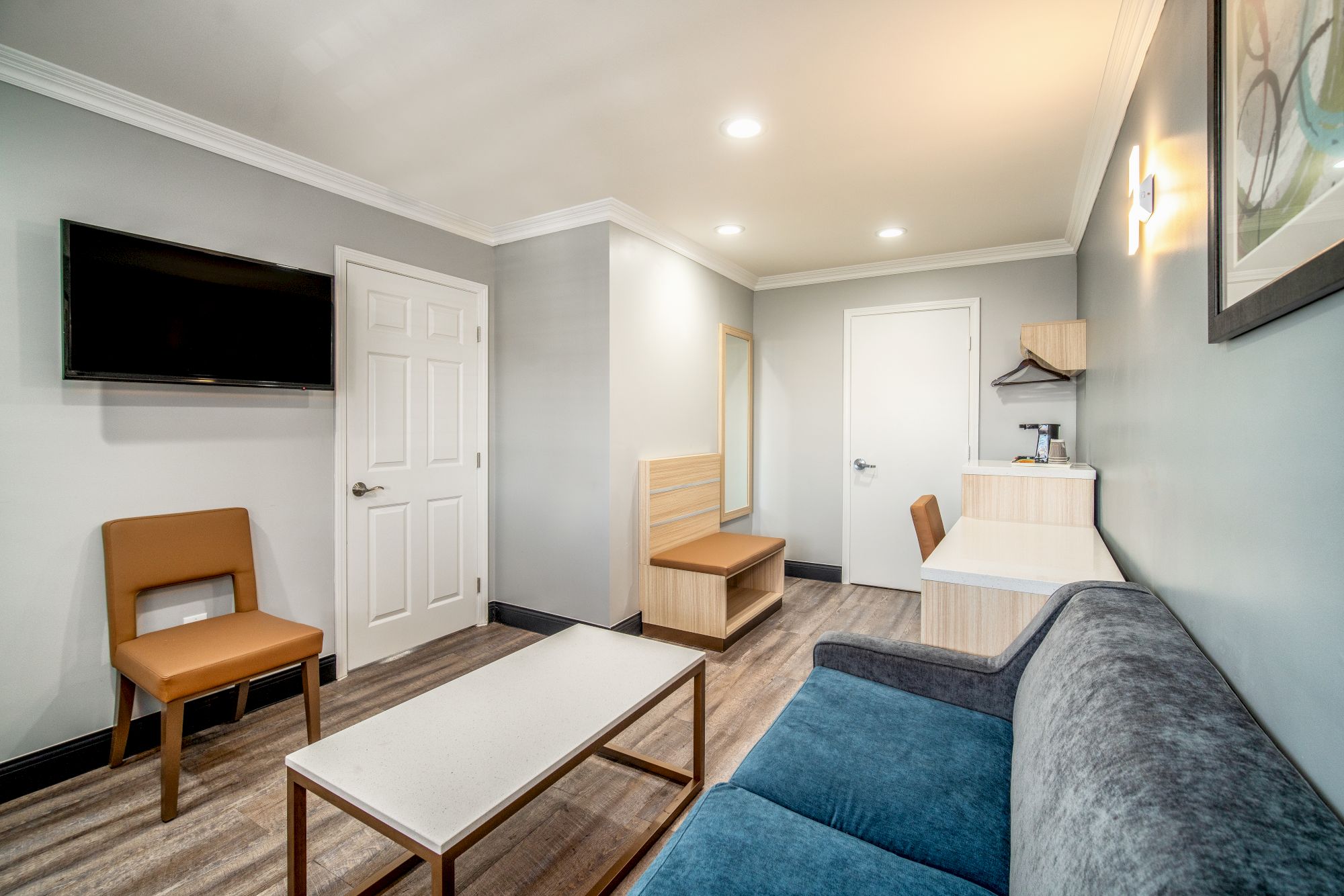 A modern living room with a TV on the wall, a door, chairs, a sofa, a coffee table, and minimalistic decor.