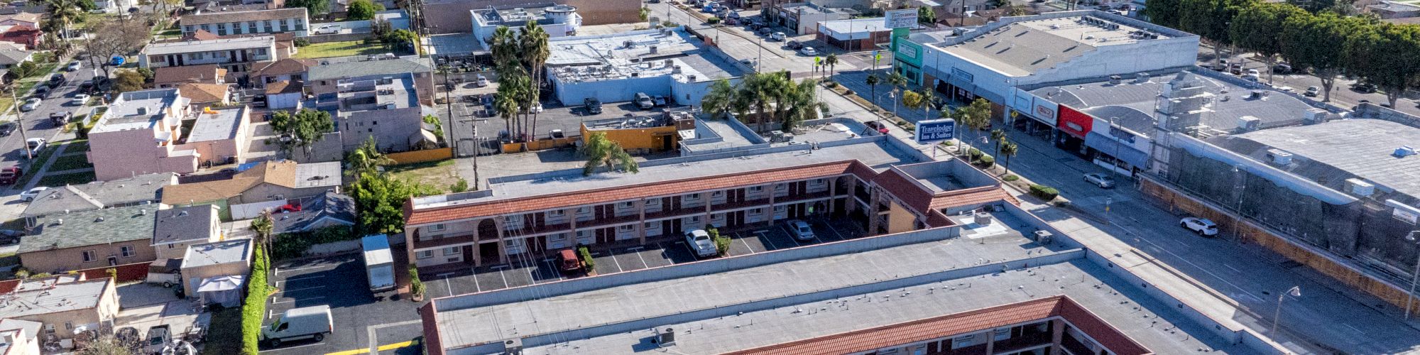 An aerial view of a neighborhood featuring buildings, roads, and parked cars under a clear blue sky.