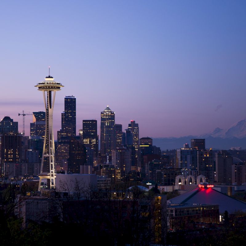 The image shows the Seattle skyline at dusk with the Space Needle prominently in view and Mount Rainier in the distance under a colorful sky.