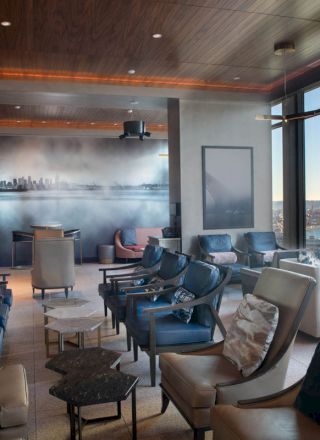 A modern lounge with numerous comfortable chairs, large windows offering a scenic view of a waterfront and Ferris wheel, and ambient lighting ends the sentence.