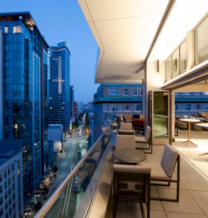 A modern cityscape at dusk, showing high-rise buildings with balconies and a sleek indoor-outdoor dining area.