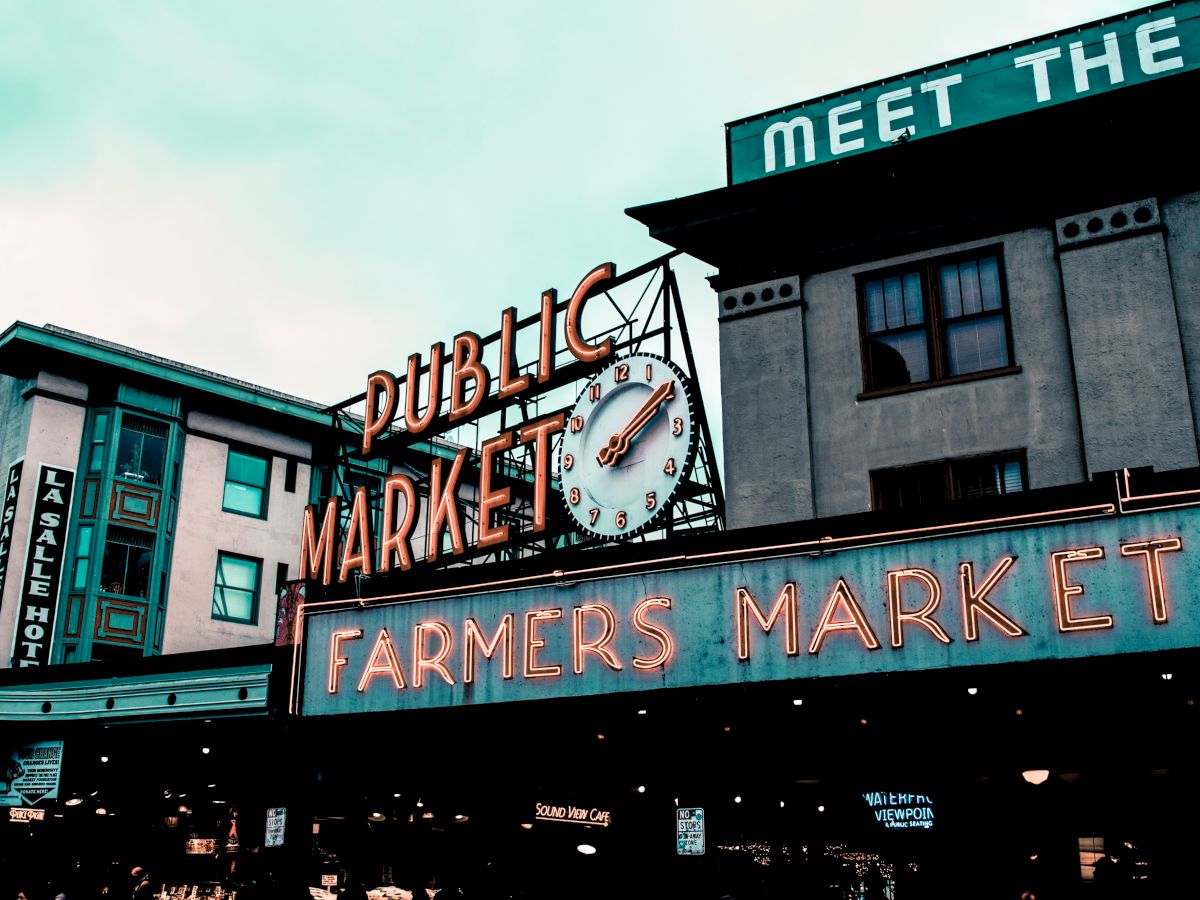 Photo of the famous Public Market Center in Seattle, highlighted by its iconic neon signs that read "PUBLIC MARKET" and "FARMERS MARKET."