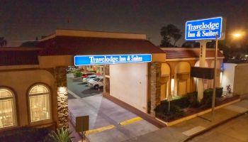 The image shows a Travelodge Inn & Suites at night, with illuminated signage and an entrance driveway.