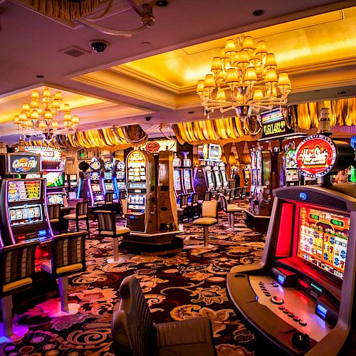 The image depicts the interior of a vibrant casino, featuring numerous slot machines, colorful lights, and chandeliers adorning the ceiling.